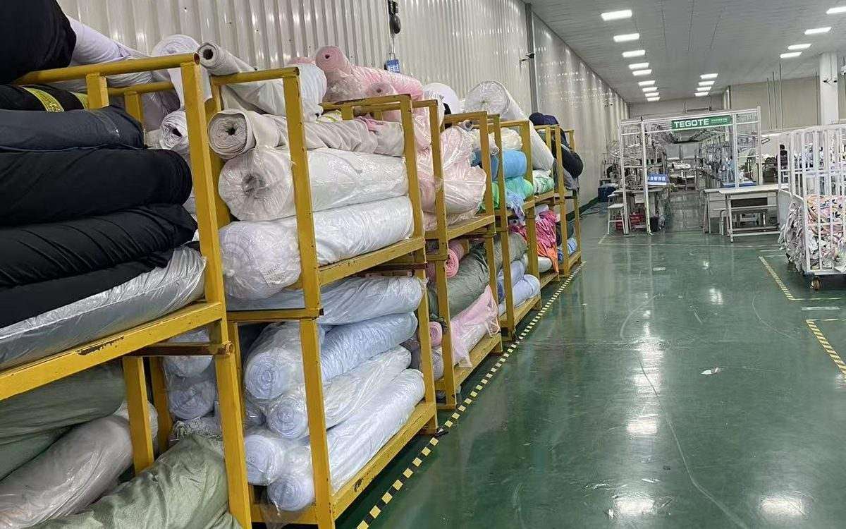 Lily Yu inspecting stocked swimwear fabric rolls in the YucaiFJ warehouse — stocked fabric is the fastest way to shorten a swimwear lead time