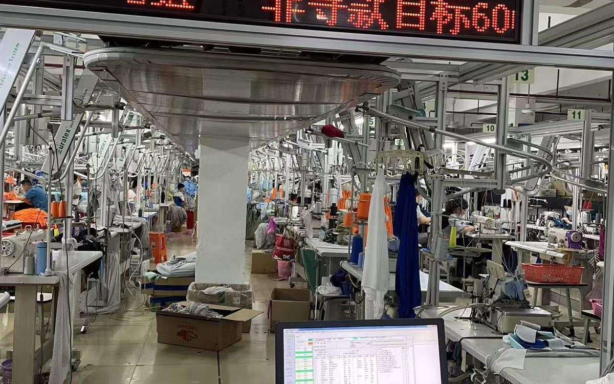 YucaiFJ factory sewing line: an operator preparing a chlorine-resistant one-piece swimsuit with flatlock seam and elastic at high stretch